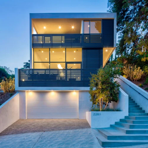 Modern two-story charcoal-grey home with wood accents, large windows and stone-lined driveway